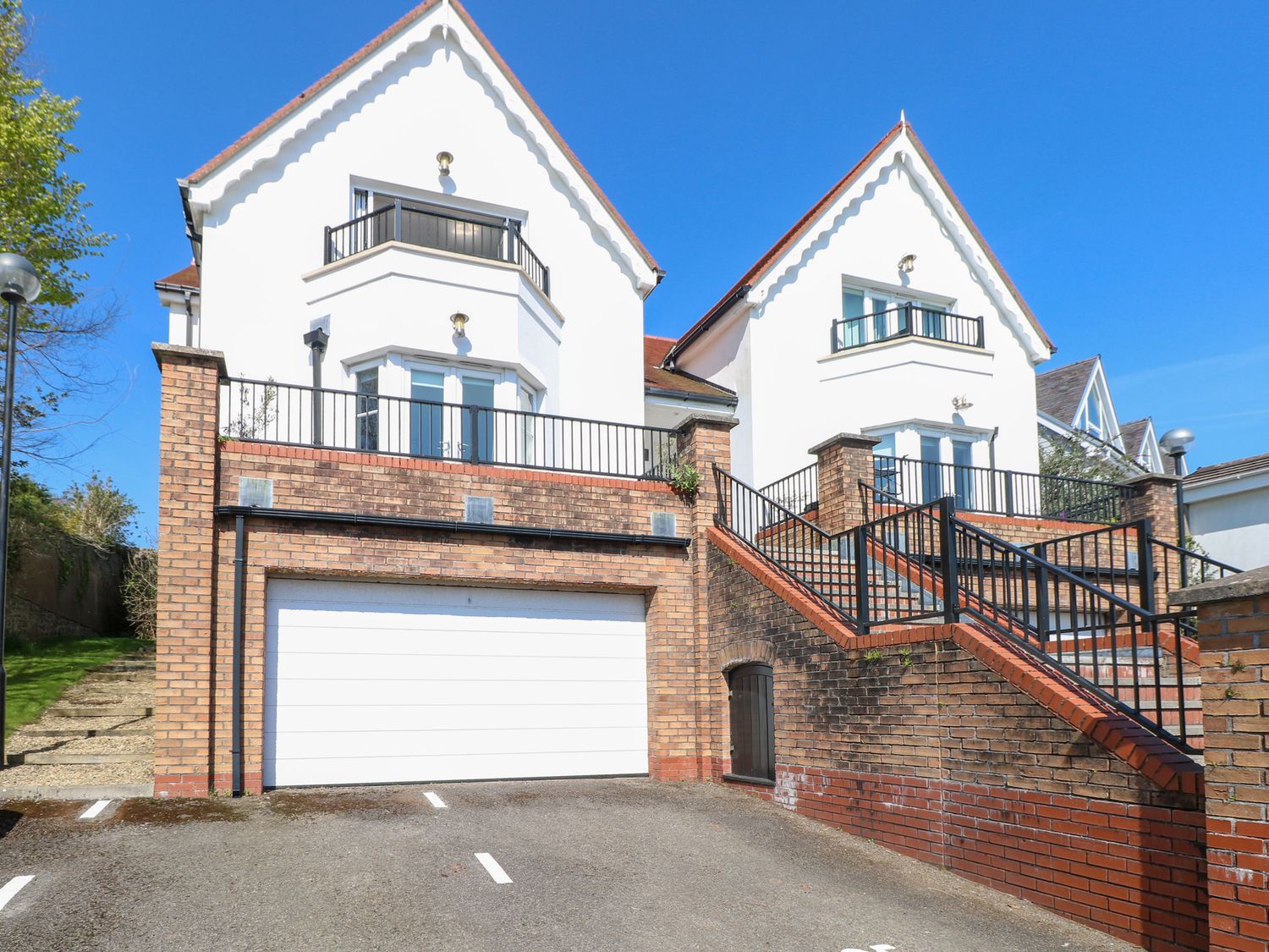 A two-story house with white walls and red roof tiles with a garage below and stairs leading up to balconies at Cambrie in Tenby