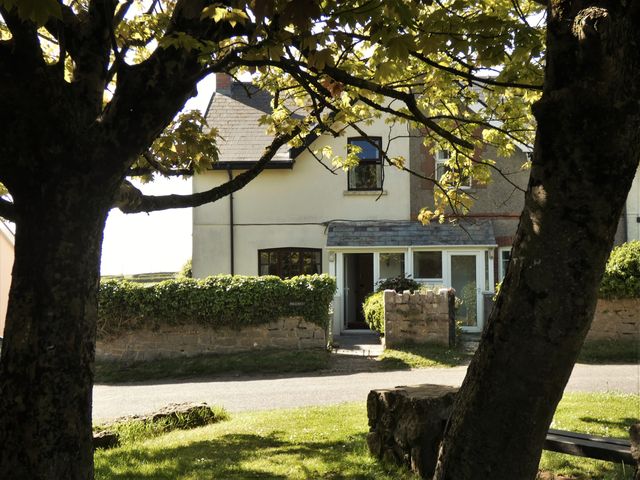 A house with a porch and garden wall viewed through two large trees at Hillcrest Oxwich near Port Eynon