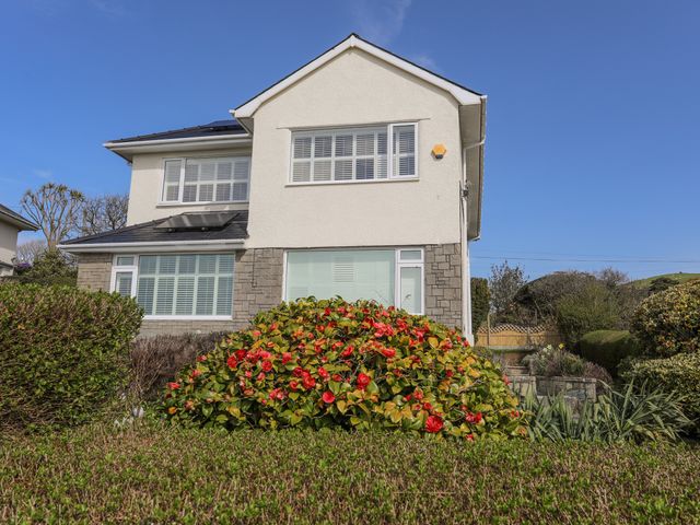 A two-story house with white walls and stone accents surrounded by shrubs and flowers at Awelfryn in Criccieth