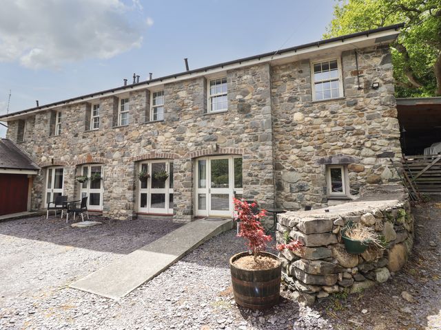 Stone exterior of a building with multiple windows and doors a small patio area with a table and chairs and a potted plant at Tryfan in Glasinfryn near Bangor
