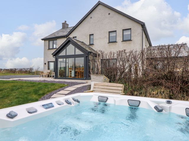 A house with a glass dining room extension a hot tub in the foreground and garden benches at Rhandir Hen in Aberystwyth