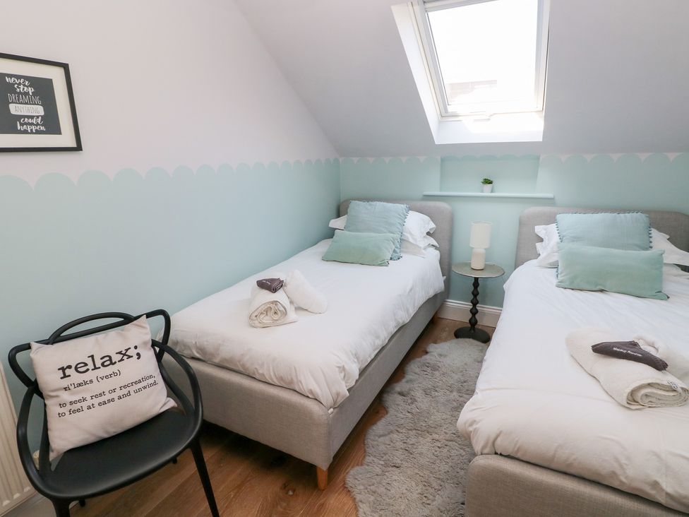 A bedroom with two single beds a black chair with a cushion a small round table with a lamp and a skylight window at Cambrie in Tenby