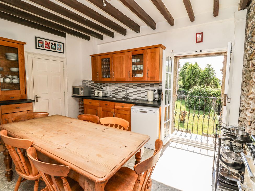 A kitchen with wooden cabinets a dining table with chairs and an open door leading to a garden at Dewi Villa in Aberarth Ceredigion