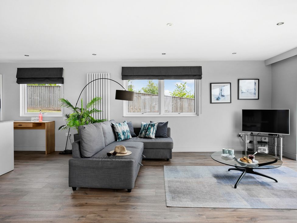 A living room with a gray sofa a glass coffee table a television and a wooden desk at Huxham View and Annex in Stoke Canon