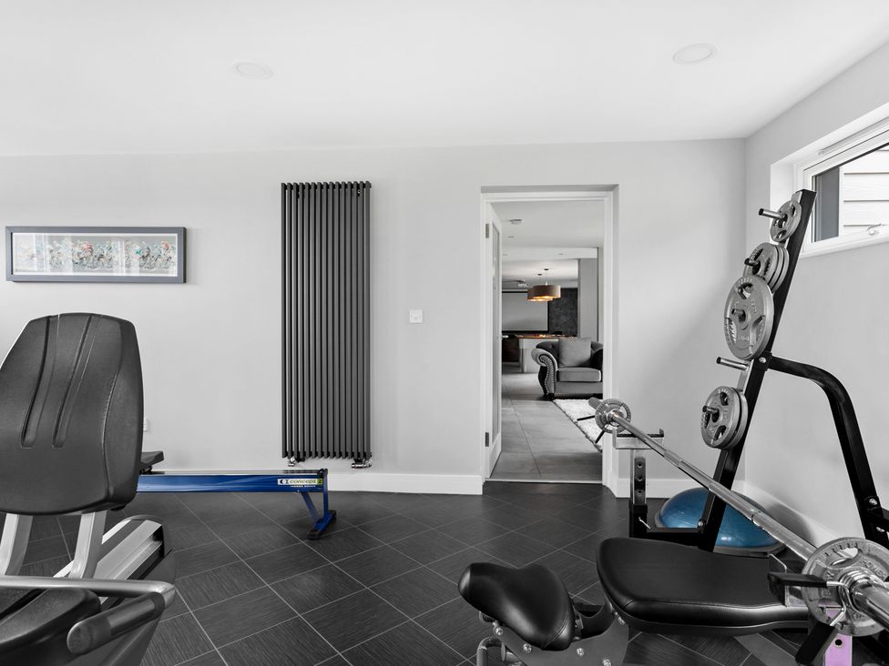 A home gym with exercise equipment and weight plates near a doorway showing a living area at Huxham View and Annex in Stoke Canon