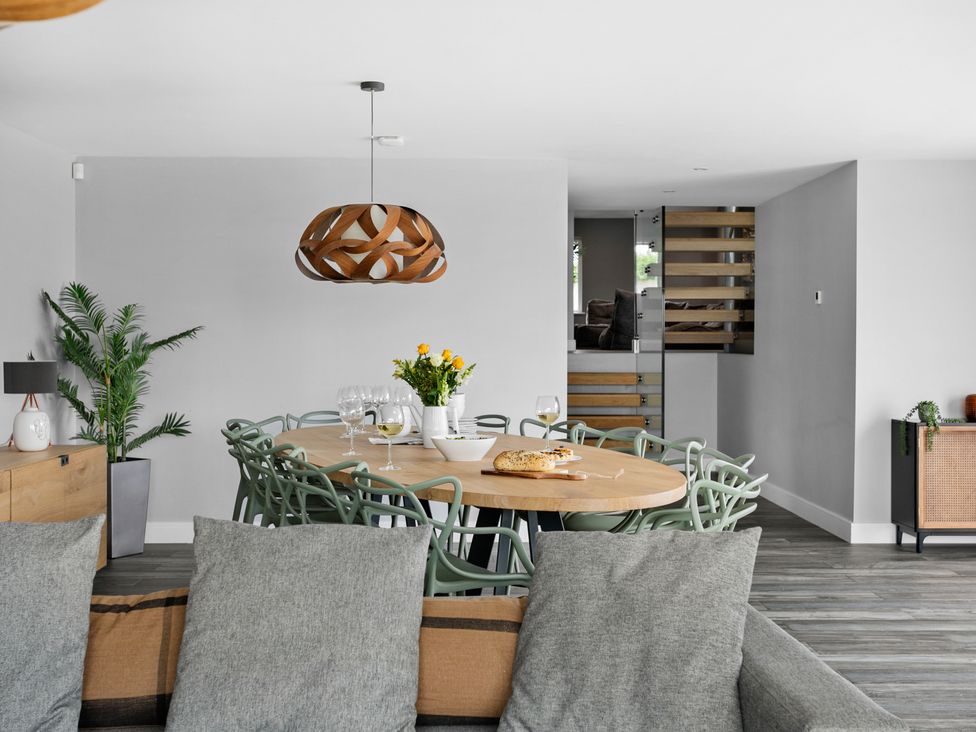 A dining area with a wooden table and green chairs and a pendant light above at Huxham View and Annex in Stoke Canon