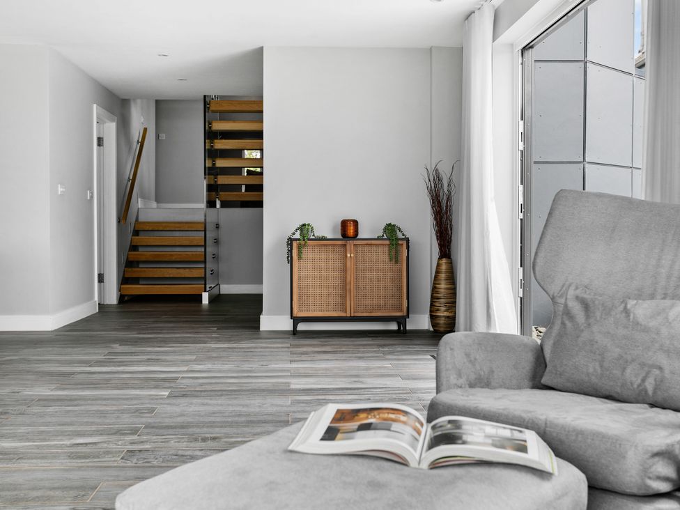 A living room with a gray armchair an open book a wooden cabinet stairs and a tall vase at Huxham View and Annex in Stoke Canon