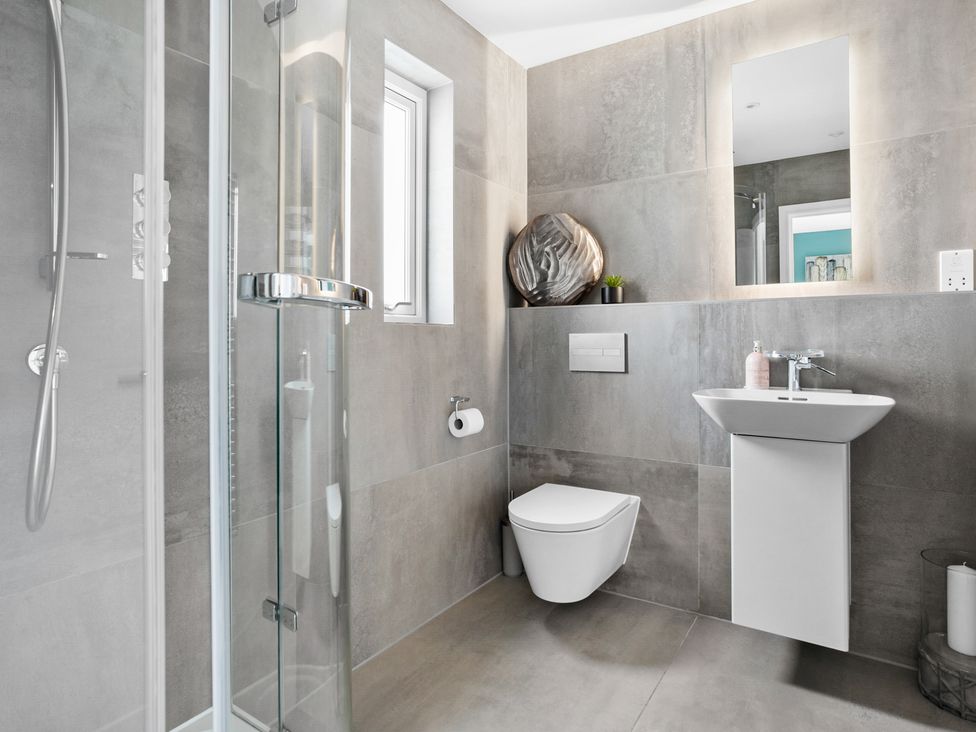 A bathroom with a wall-mounted toilet a sink with a mirror and a glass shower enclosure at Huxham View and Annex in Stoke Canon