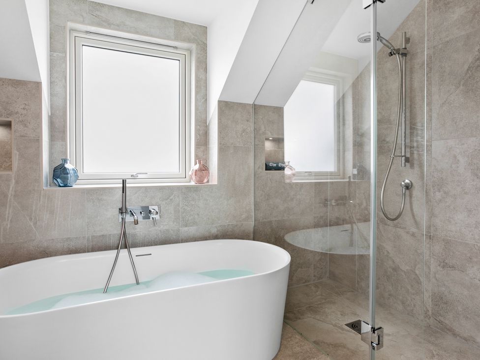 A bathroom with a freestanding bathtub filled with water and foam and a walk-in glass shower at Huxham View and Annex in Stoke Canon