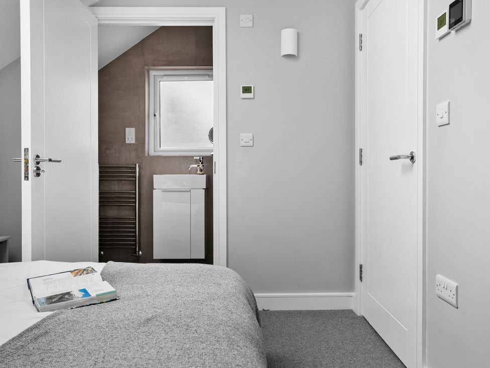 A bedroom with a gray blanket on the bed and a view into a bathroom with a sink and towel rack at Huxham View and Annex in Stoke Canon