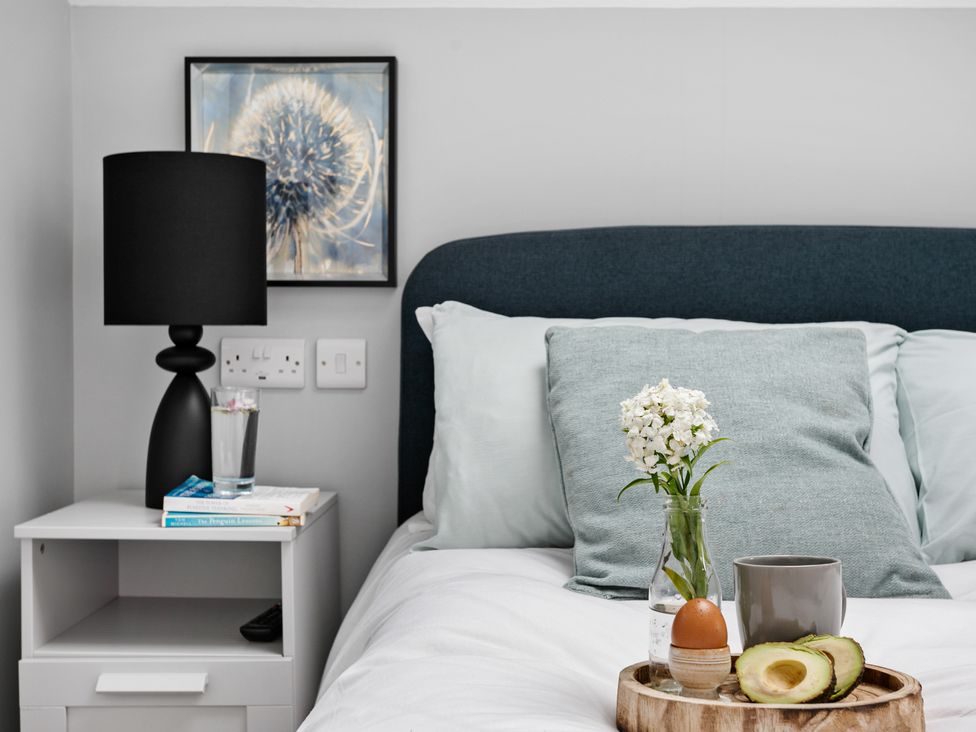 A bedroom with a bedside table holding a black lamp books and a glass of water at Huxham View and Annex in Stoke Canon