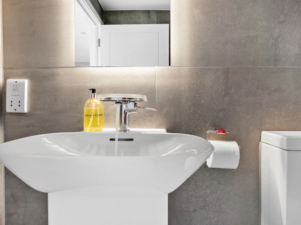 A bathroom sink with running water a hand soap dispenser a toilet paper holder and a toilet at Huxham View and Annex in Stoke Canon