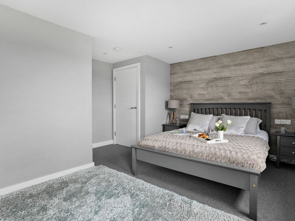 A bedroom with a gray bed frame a textured wall behind the bed bedside tables with lamps and a tray with food on the bed at Huxham View and Annex in Stoke Canon