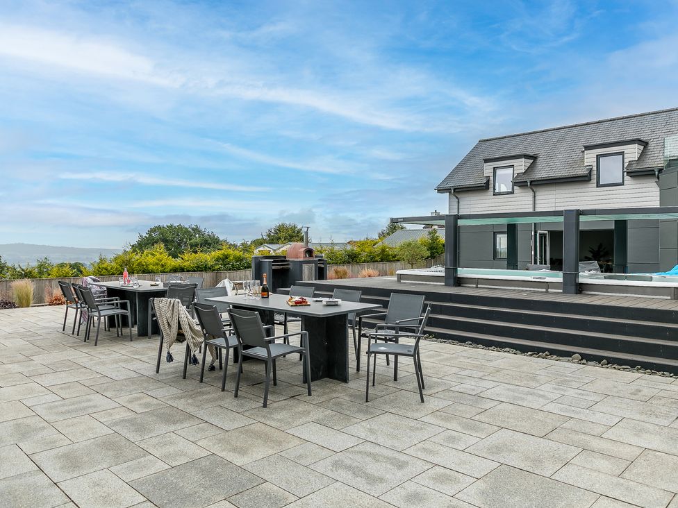 An outdoor patio area with two dining tables and chairs near a modern house at Huxham View and Annex in Stoke Canon