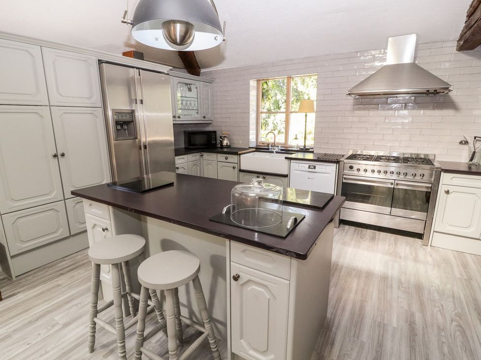 A kitchen with an island and stools stainless steel appliances and a window showing outside at Mickle Trafford Manor in Chester
